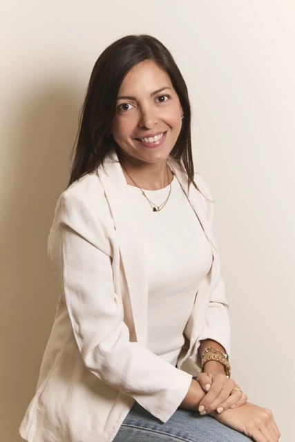 Yasmin Morales sentada, con blazer crema y las manos sobre las rodillas.